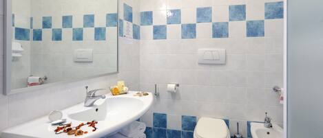 A bathroom with a white sink, mirror, and two sinks; a toilet and bidet; blue and white tiled walls; and a towel rack.