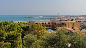 Un pueblo costero con edificios cerca del mar, un faro y un rompeolas rocoso.