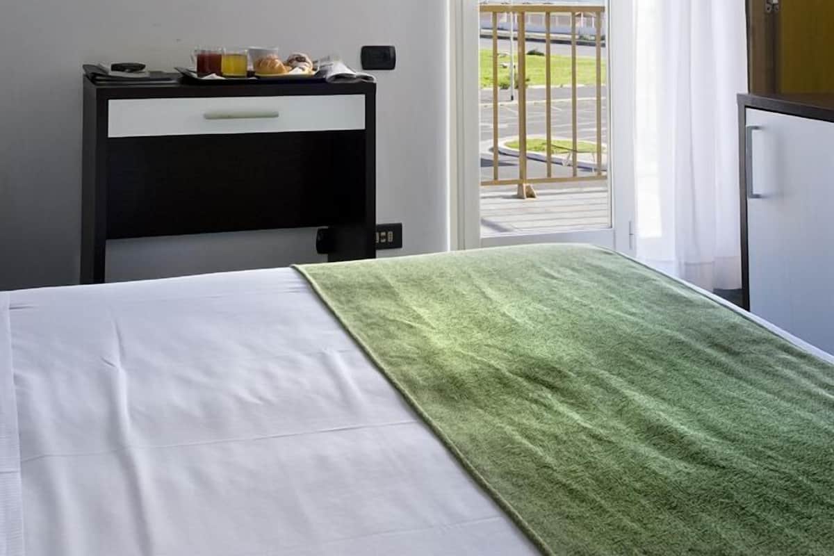 Habitació d'hotel amb un llit, una taula de nit amb una làmpada, una finestra amb cortines i vista a l'exterior.