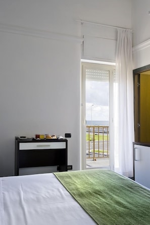 A hotel room with a bed, a bedside table with a lamp, a window with curtains, and a view of the outside.