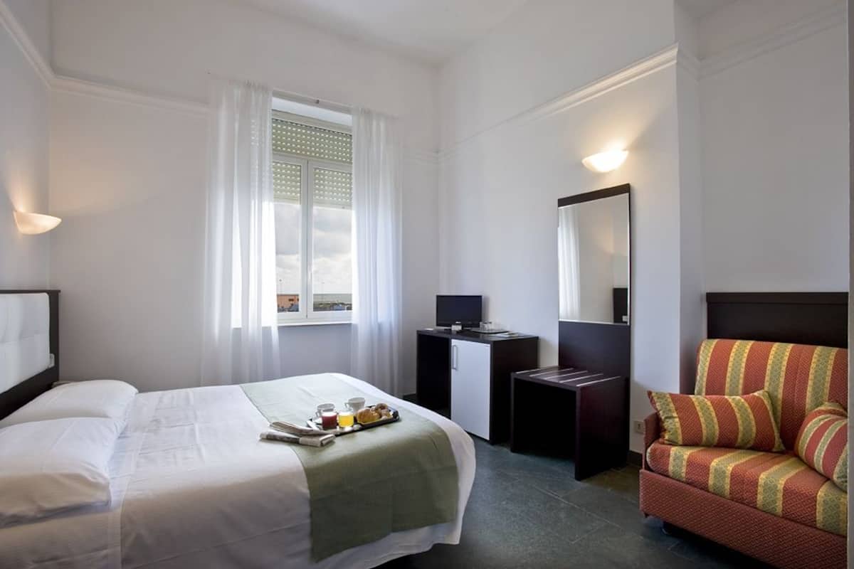 Habitació d'hotel amb un llit, una taula de treball, una cadira, una finestra amb cortines i un mirall.