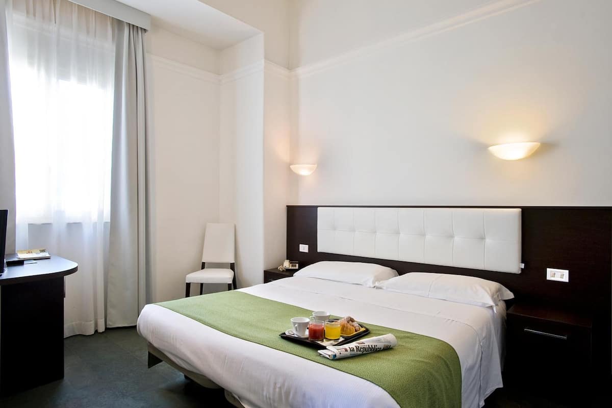 Habitació d'hotel amb llit, taulell de nit, cadira i escriptori amb cadira.
