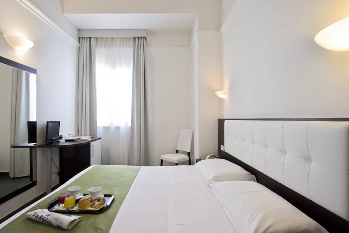 Habitació d'hotel amb un llit, escriptori amb ordinador, cadira i safata amb menjar per esmorzar.