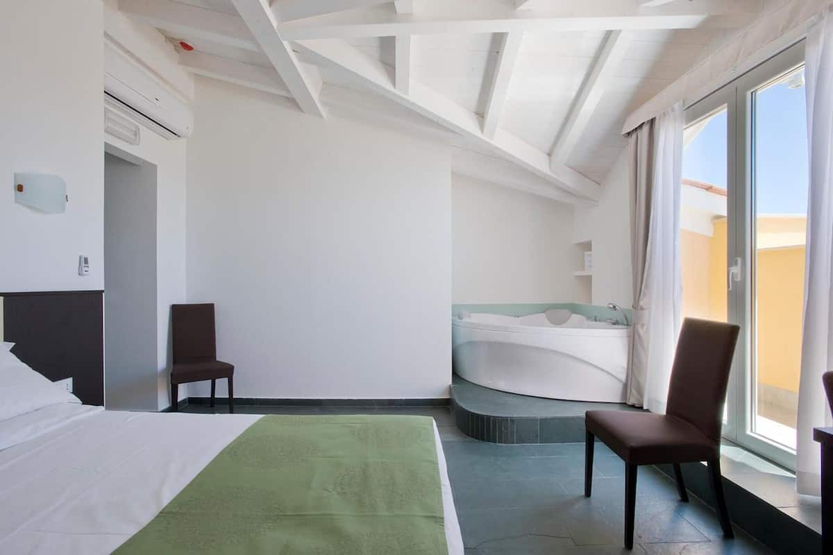 Habitació d'hotel amb un llit, dues cadires, una banyera i un finestral gran.