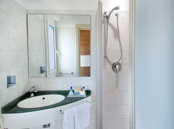Un baño moderno con un espejo grande, un lavamanos con artículos de tocador y una ducha.
