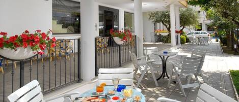 An outdoor seating area with white chairs and tables, a newspaper, and a drink.