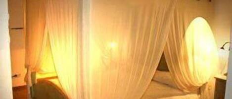 Una cama individual con dosel, una mesita de noche y una lámpara fijada a la pared.