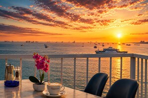 Vista al atardecer desde un balcón con una mesa, sillas, una taza de café y una planta en maceta.