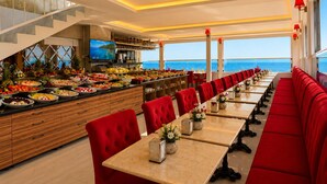 Un restaurante con una barra larga, asientos tapizados en rojo y vista al mar.