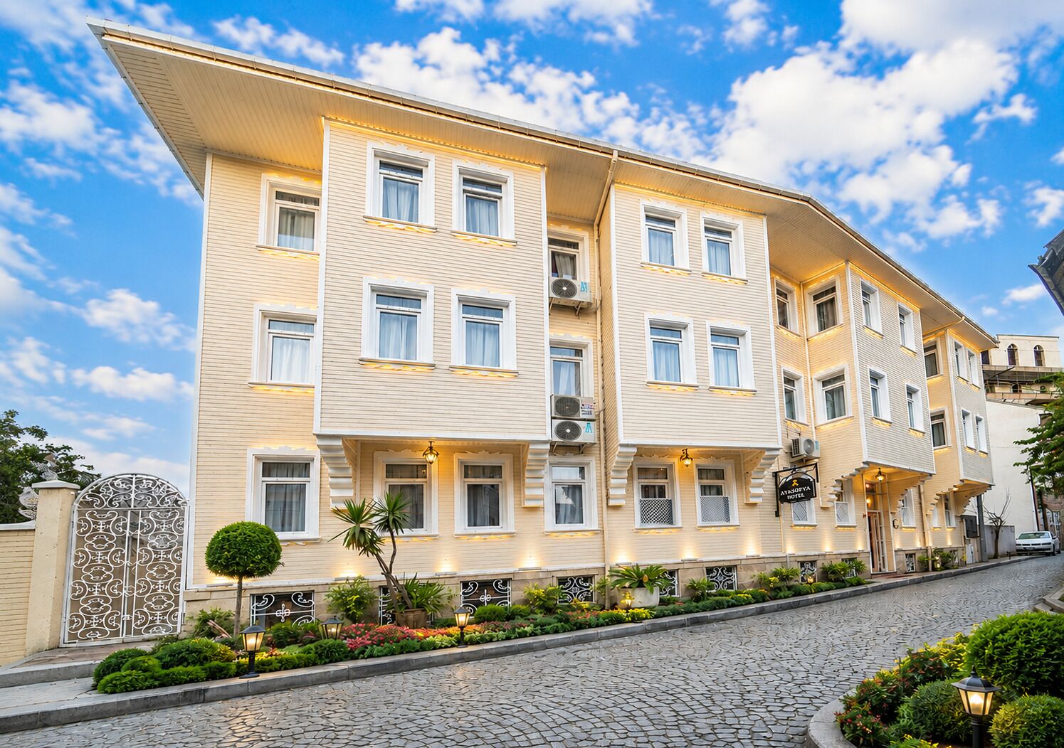 A multi-story hotel with a symmetrical facade, multiple windows, and a well-maintained garden with a cobblestone pathway.