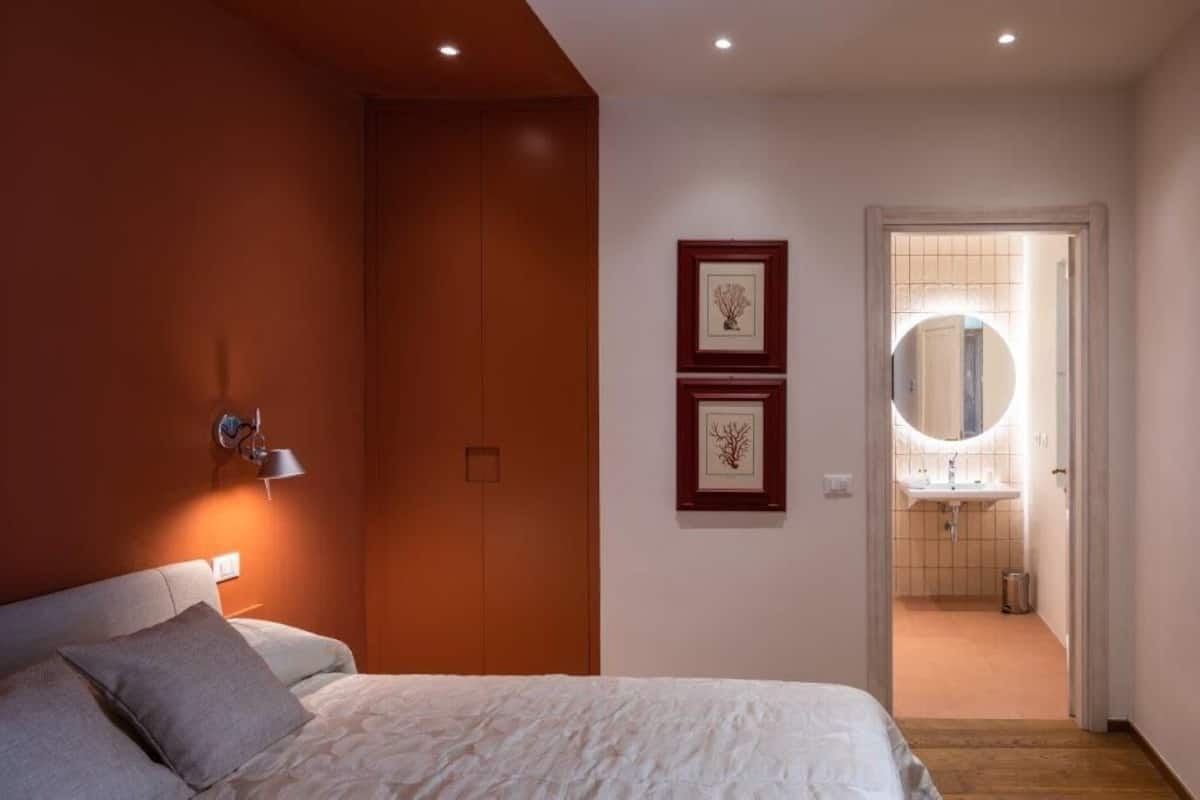 Una camera da letto con un letto, una lampada da comodino, un armadio e un bagno parzialmente visibile attraverso una porta aperta.