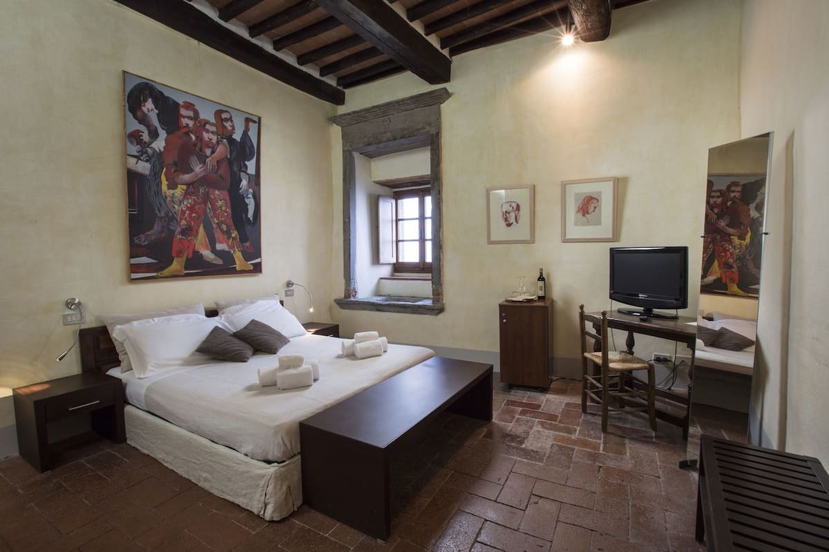Una camera da letto con un letto, comodini, una scrivania con una sedia, una televisione e opere d'arte alle pareti.