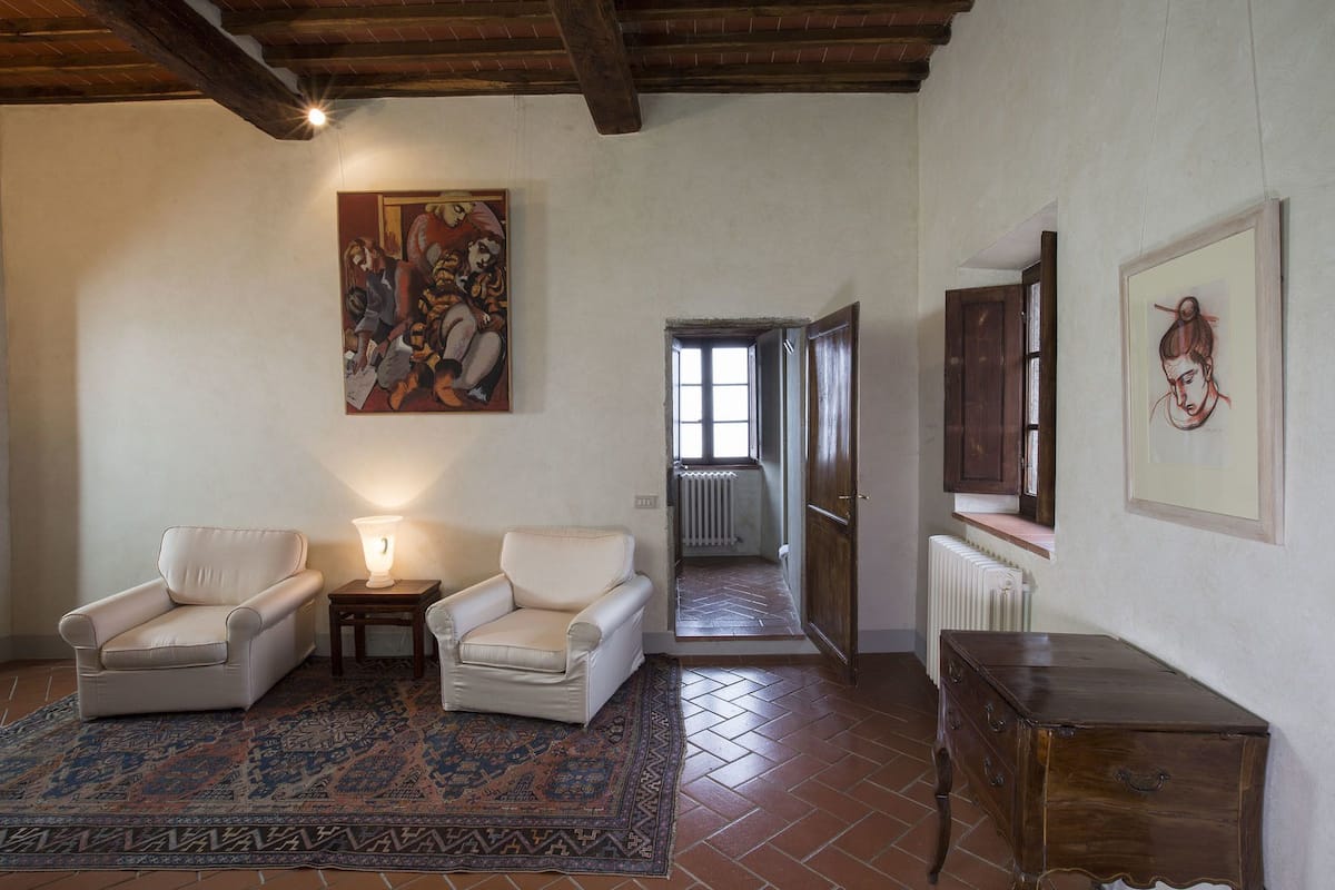 Una stanza con due poltrone bianche, un tappeto decorato, un mobiletto in legno e opere d'arte alle pareti.