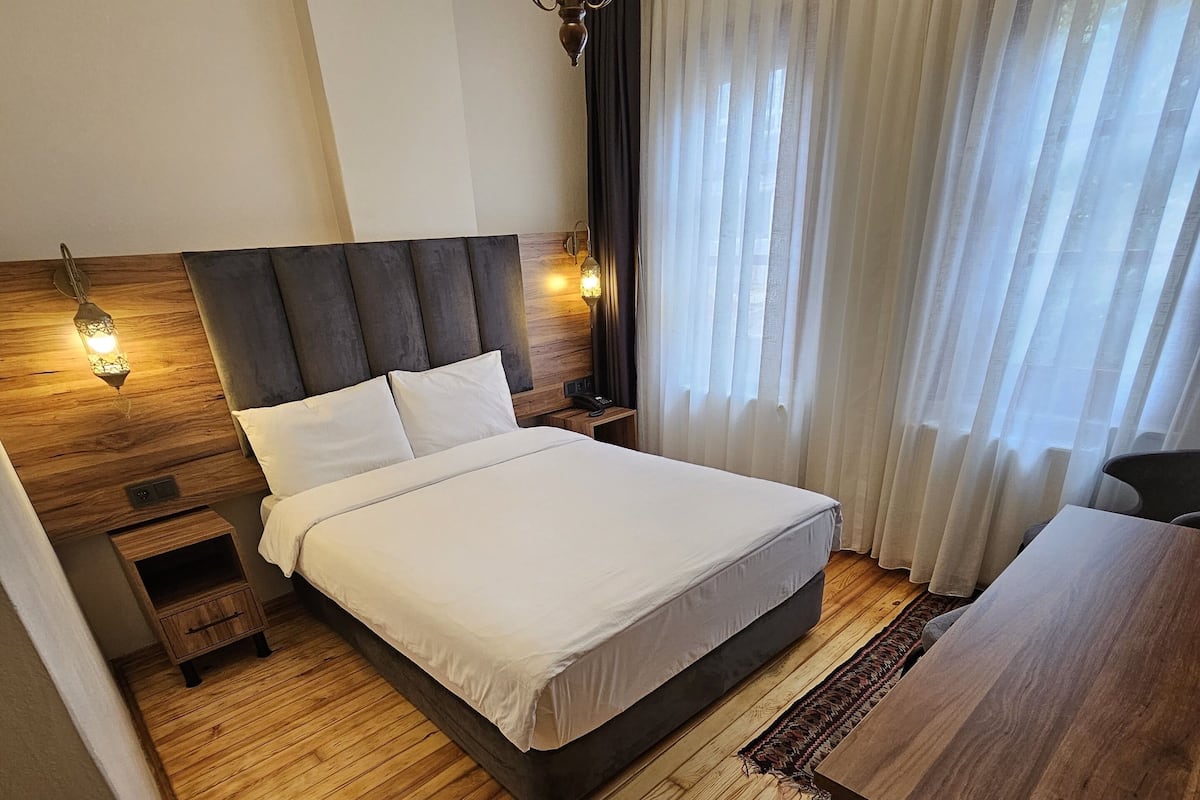 Une chambre d’hôtel moderne avec un grand lit, un plancher en bois, une tête de lit en bois, une table de chevet, un bureau et un lustre.