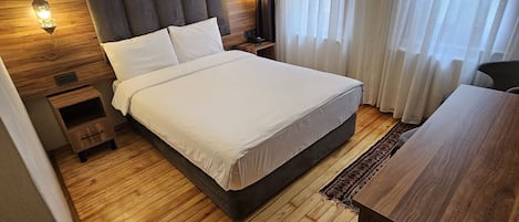Una habitación de hotel moderna con una cama grande, suelo de madera, cabecero de madera, una mesita de noche, un escritorio y una araña.