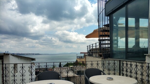 Un balcon avec deux tables rondes et des chaises, d’où l’on peut admirer un plan d’eau et une vue lointaine sur la ville.