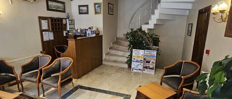 A lobby with a reception desk, seating area, staircase, and decorative lighting.