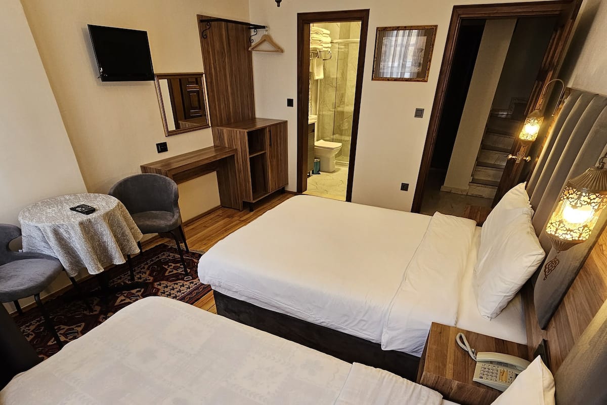 Une chambre d’hôtel avec deux lits, un bureau, une chaise, une télévision et une salle de bain visible à travers une porte ouverte.