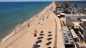 Ein Hotel am Strand mit einer langen Terrasse mit Blick auf das Meer, Liegestühlen und Sonnenschirmen.