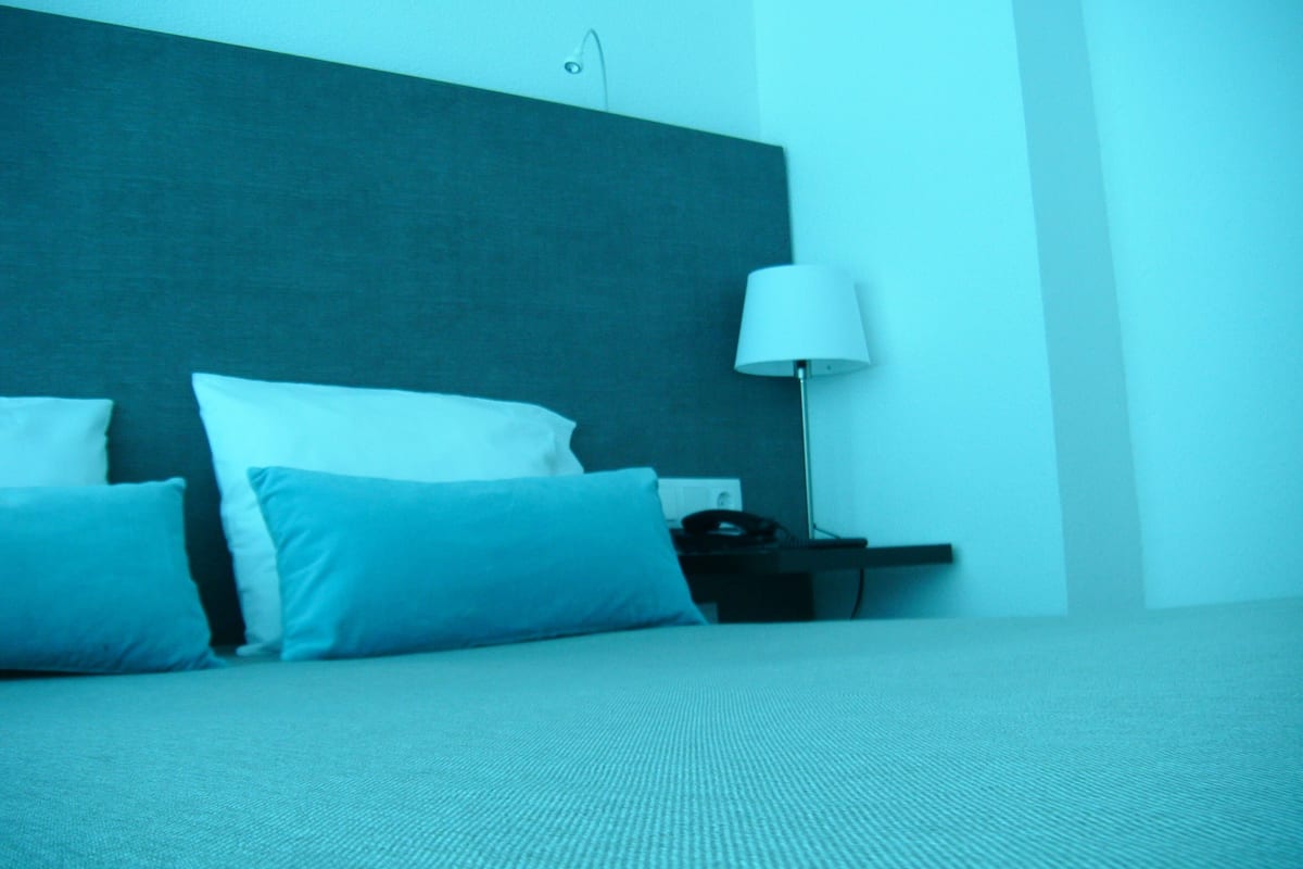 Une chambre d’hôtel avec un lit, des oreillers, une table de chevet et une lampe.