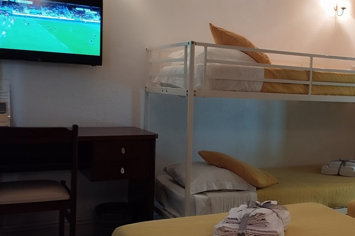 Une chambre avec des lits superposés, un bureau et un téléviseur diffusant un événement sportif.