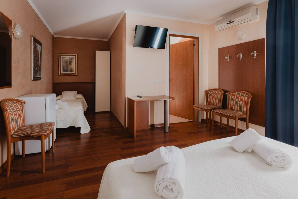 Una habitación de hotel con cama, escritorio, dos sillas, televisor y armario.