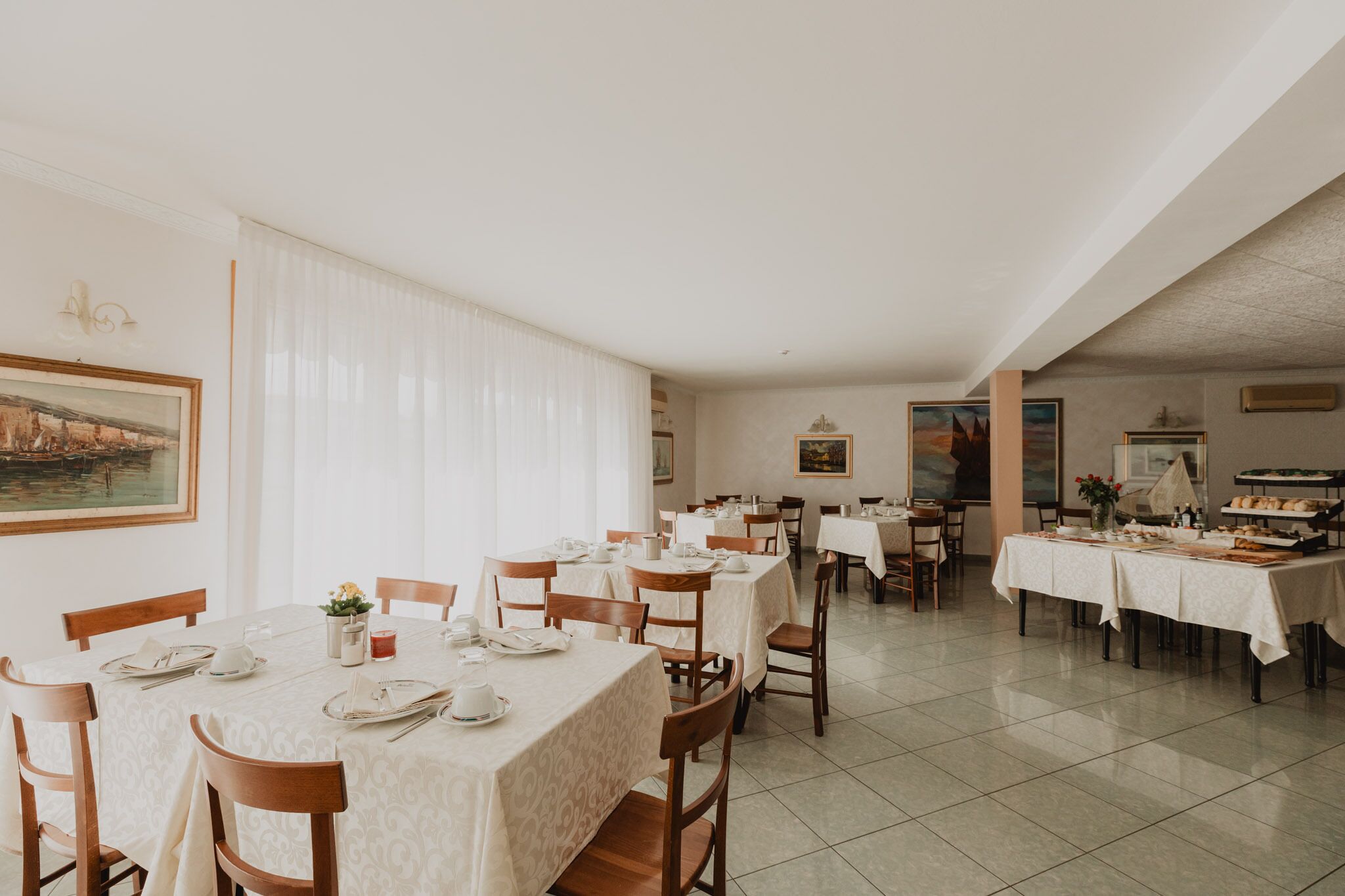 A dining area with tables set for service, a buffet line, and a painting on the wall.