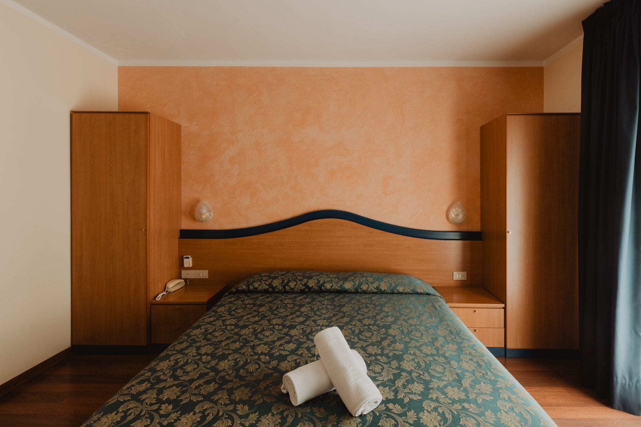 Una habitación de hotel con una cama, un armario de madera, una mesita de noche con una lámpara y un teléfono.