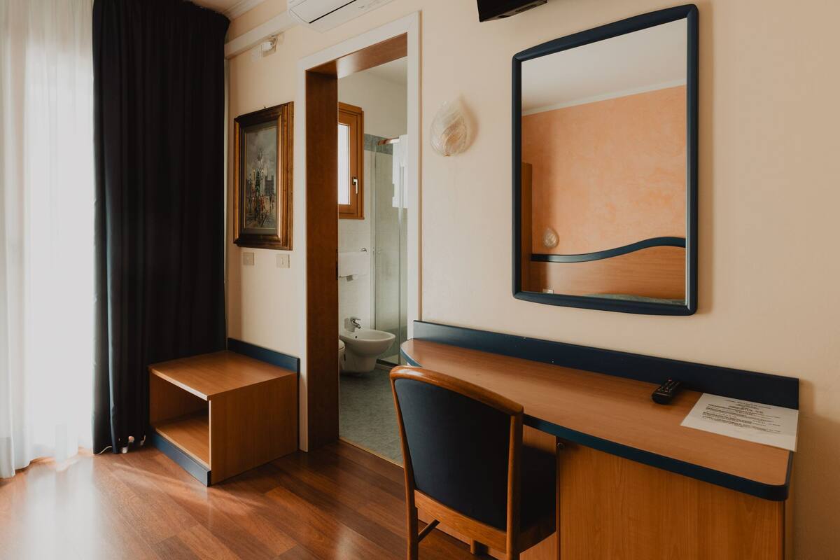 Habitación de hotel con escritorio de madera, una silla, un espejo grande y un cuadro en la pared.