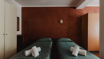 A room with two beds, each with a patterned bedspread and a rolled towel.