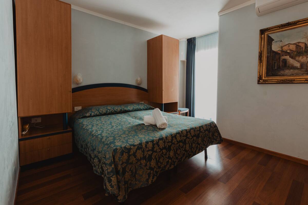 Una habitación de hotel con cama, armario de madera y un cuadro en la pared.