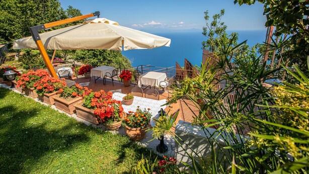 An outdoor patio with a table and chairs, surrounded by potted plants and flowers. - Nido degli Dei (Agerola)