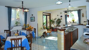 A dining area with tables and chairs, a kitchen area with a counter and sink, and a view of the outdoors. - Nido degli Dei (Agerola)