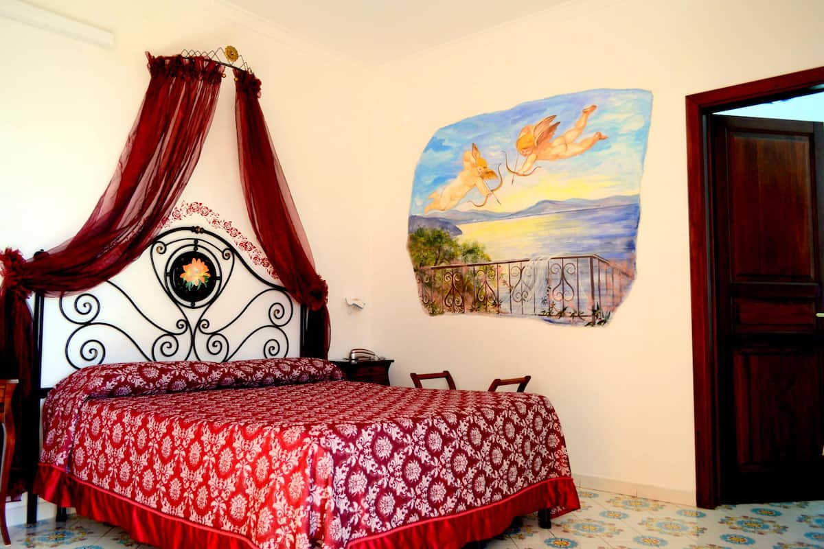 A bedroom with a four-poster bed, a mural of flying angels, and a view of a balcony.