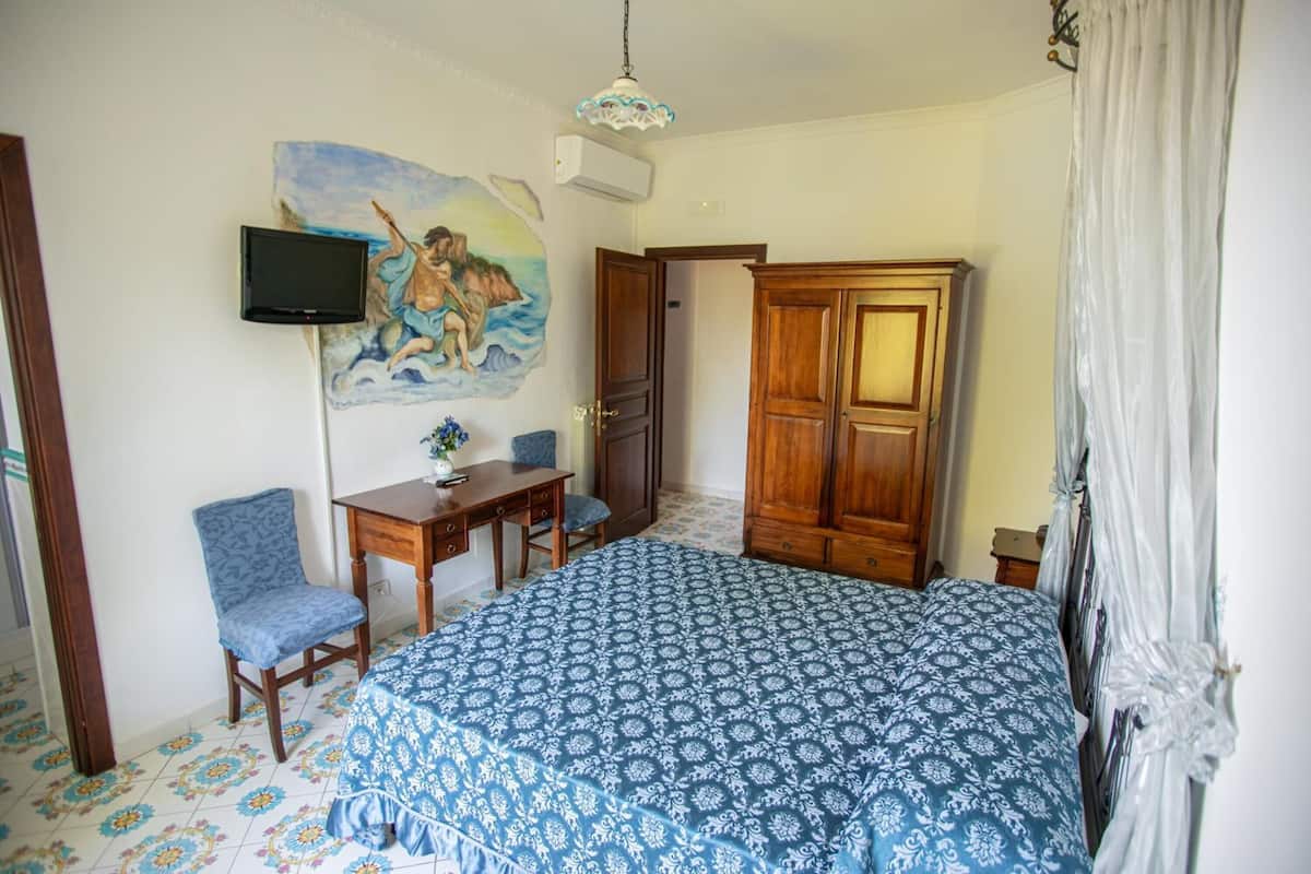 A bedroom with a bed, a desk, a chair, a television mounted on the wall, and a wardrobe.