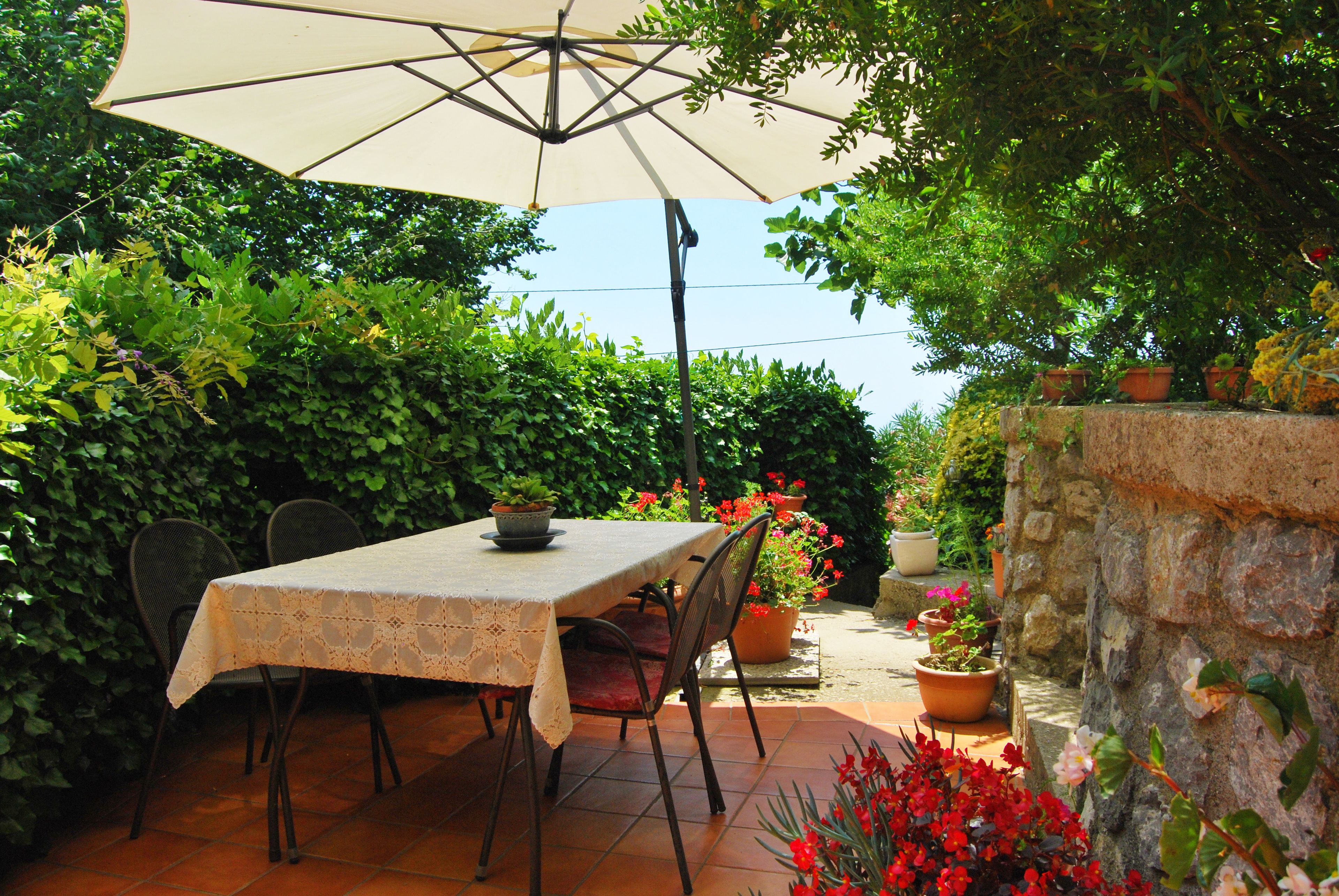 An outdoor patio with a table and chairs, surrounded by potted plants and a stone wall.