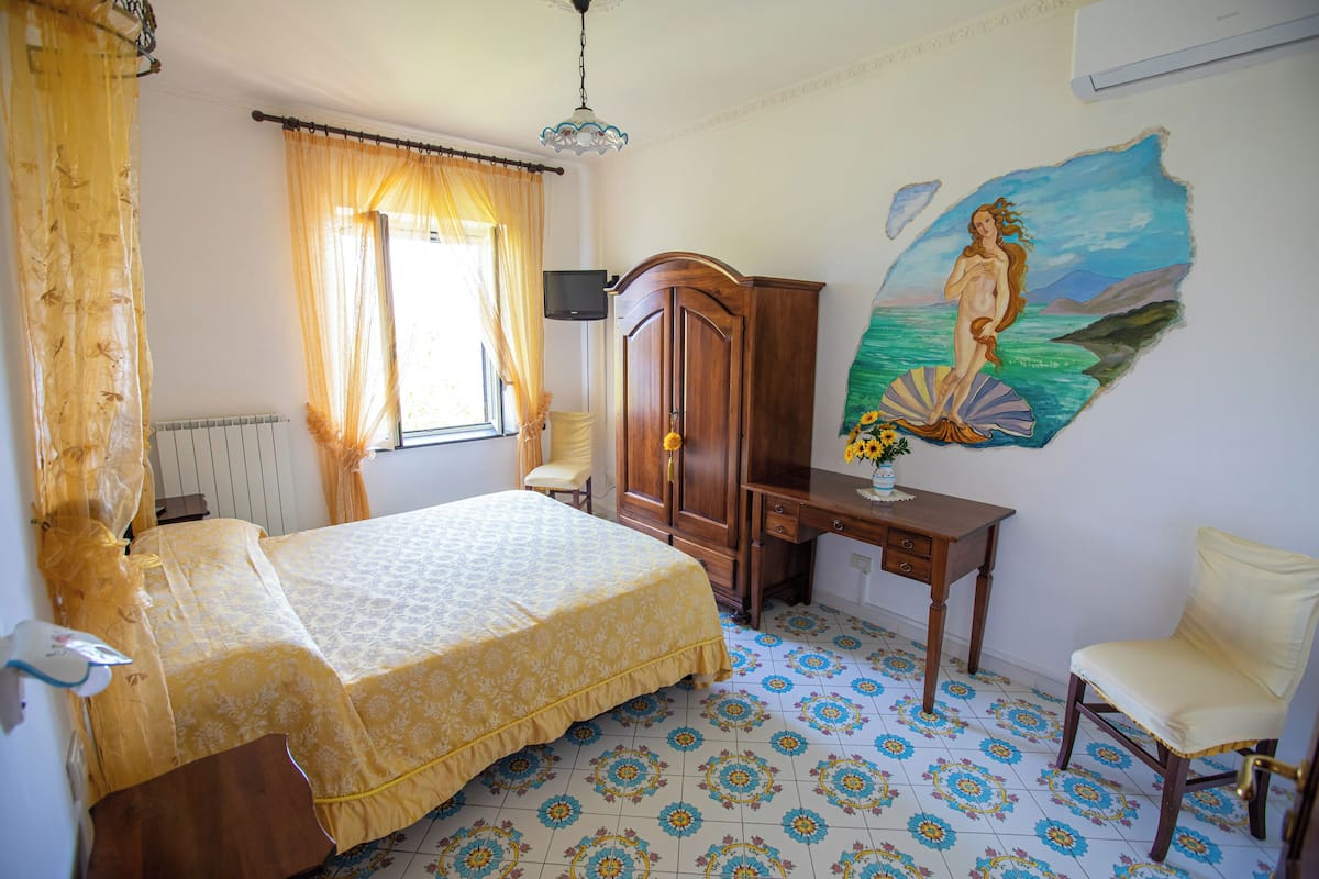A bedroom with a bed, a desk, a chair, a wardrobe, and a mural on the wall.