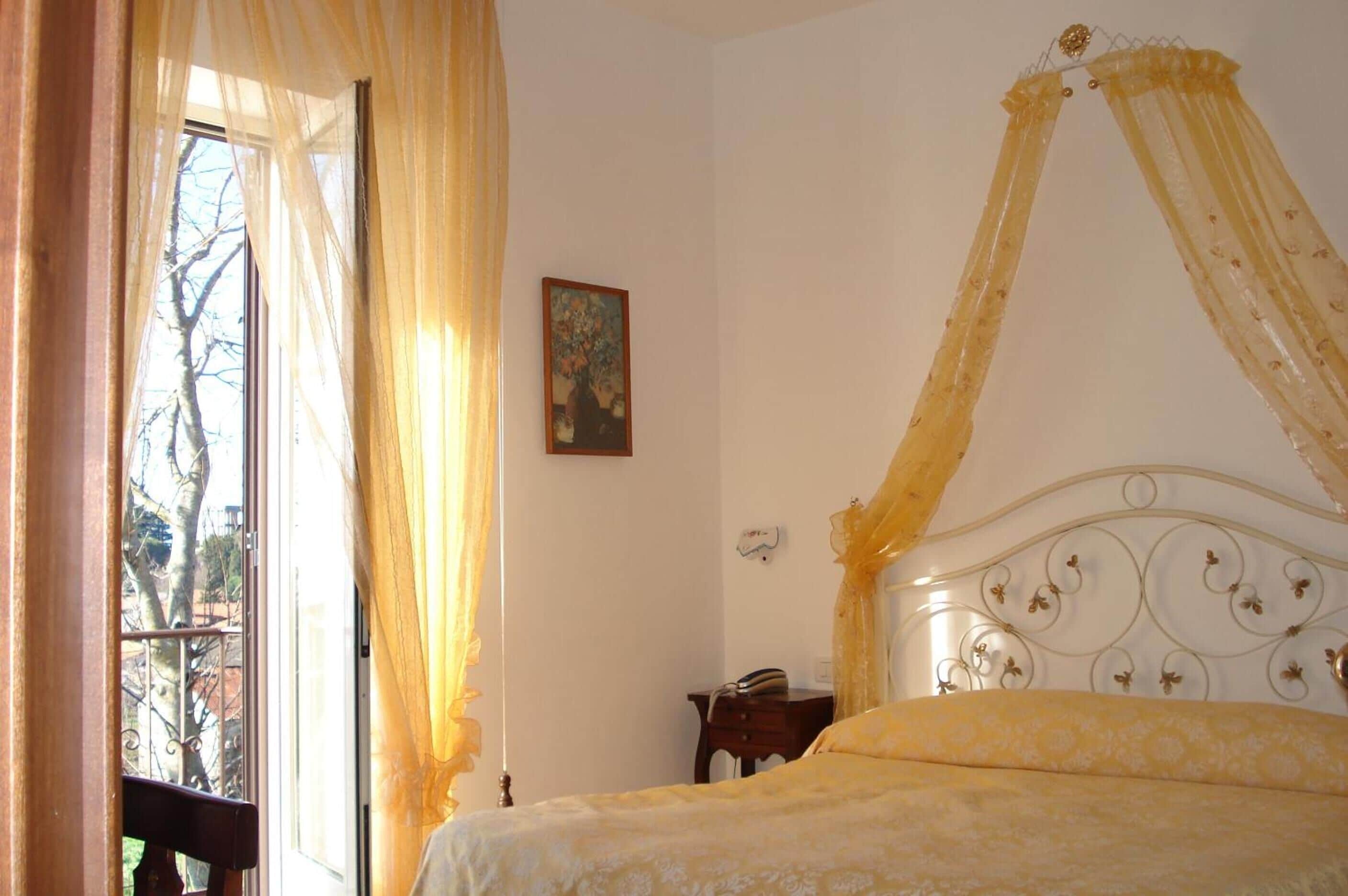 Une chambre à coucher avec un lit à baldaquin, une fenêtre avec des rideaux, une petite table de chevet et un tableau au mur.