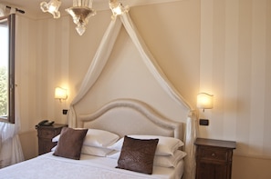 A bedroom with a canopy bed, bedside lamps, a nightstand, and a window with curtains.