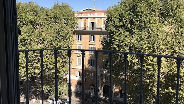 A balcony with a view of a building with multiple windows and balconies, surrounded by trees. - Il Tesoro (Rome)