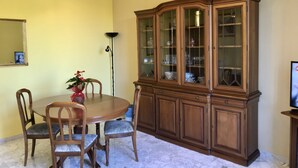 A dining room with a round table, four chairs, a wooden cabinet with glass doors, a chandelier, and a floor lamp. - Il Tesoro (Rome)