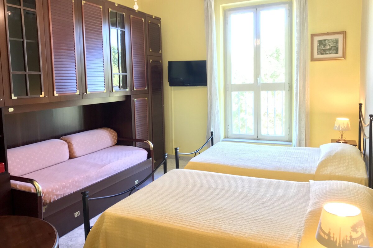 A hotel room with two beds, a TV mounted on the wall, and a large window with curtains.
