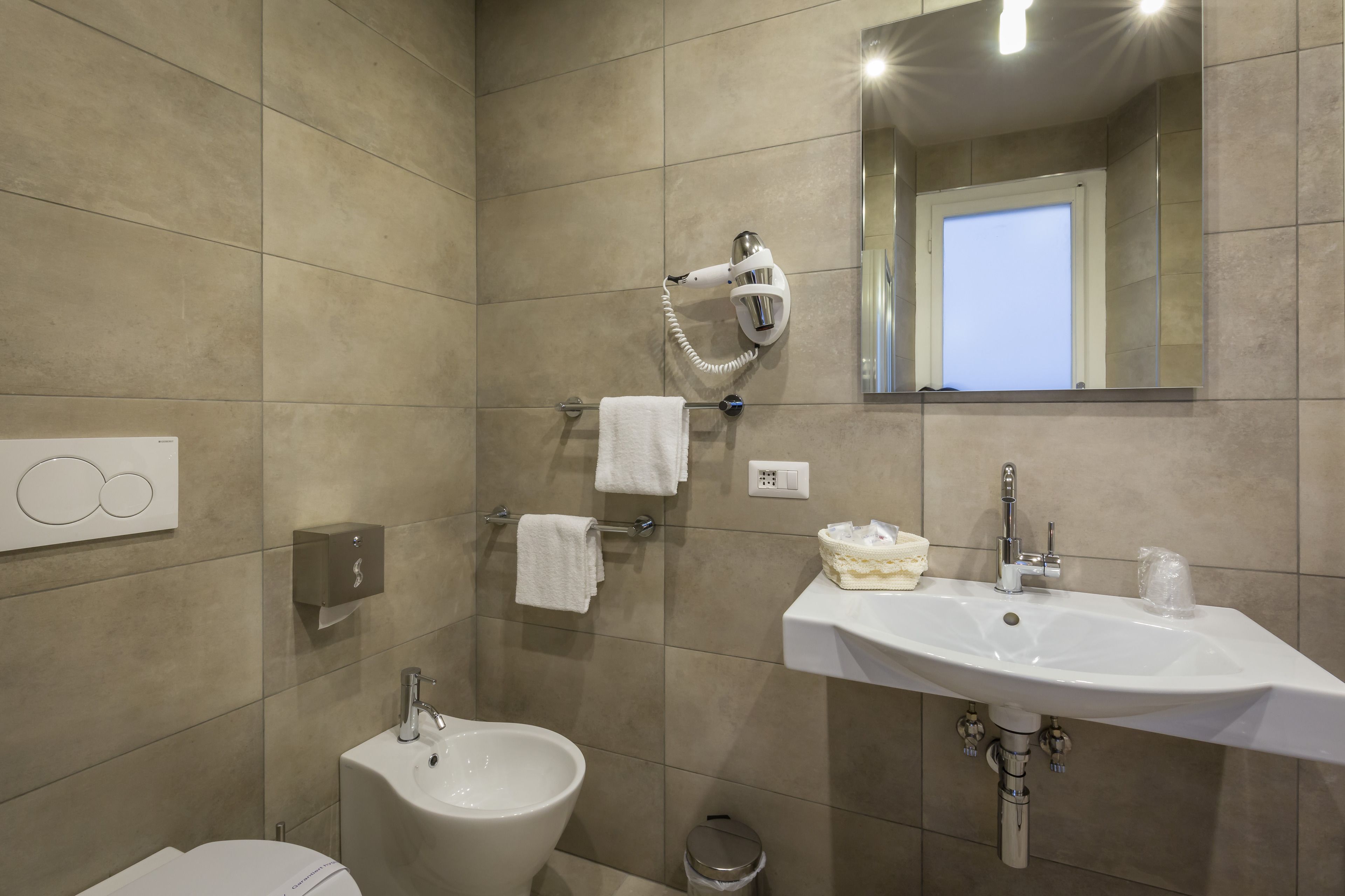 Un baño moderno con un bidé, un lavamanos y un secador de pelo montado en la pared.