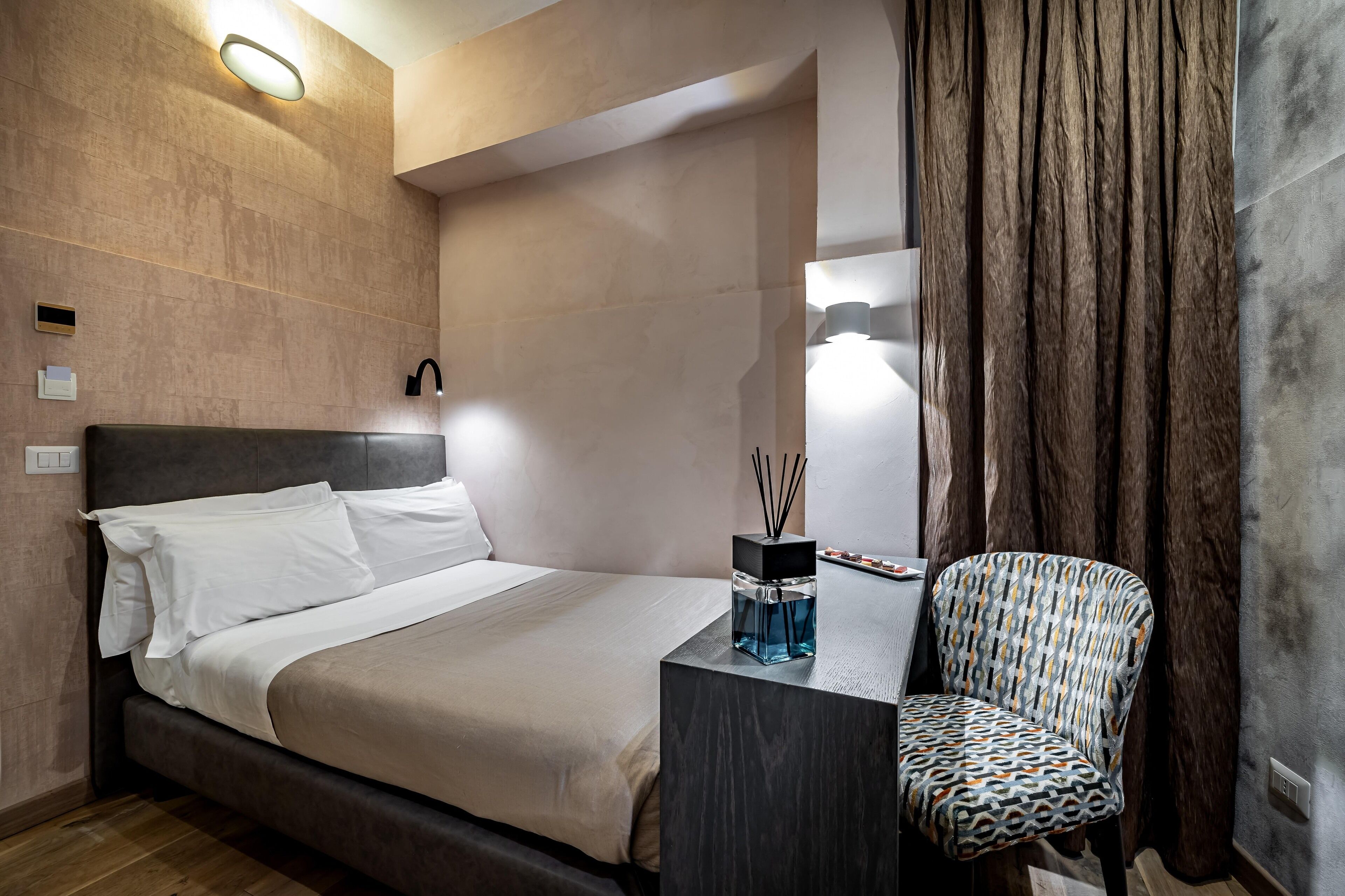 A modern hotel room with a large bed, a nightstand, a chair, and a mirror.