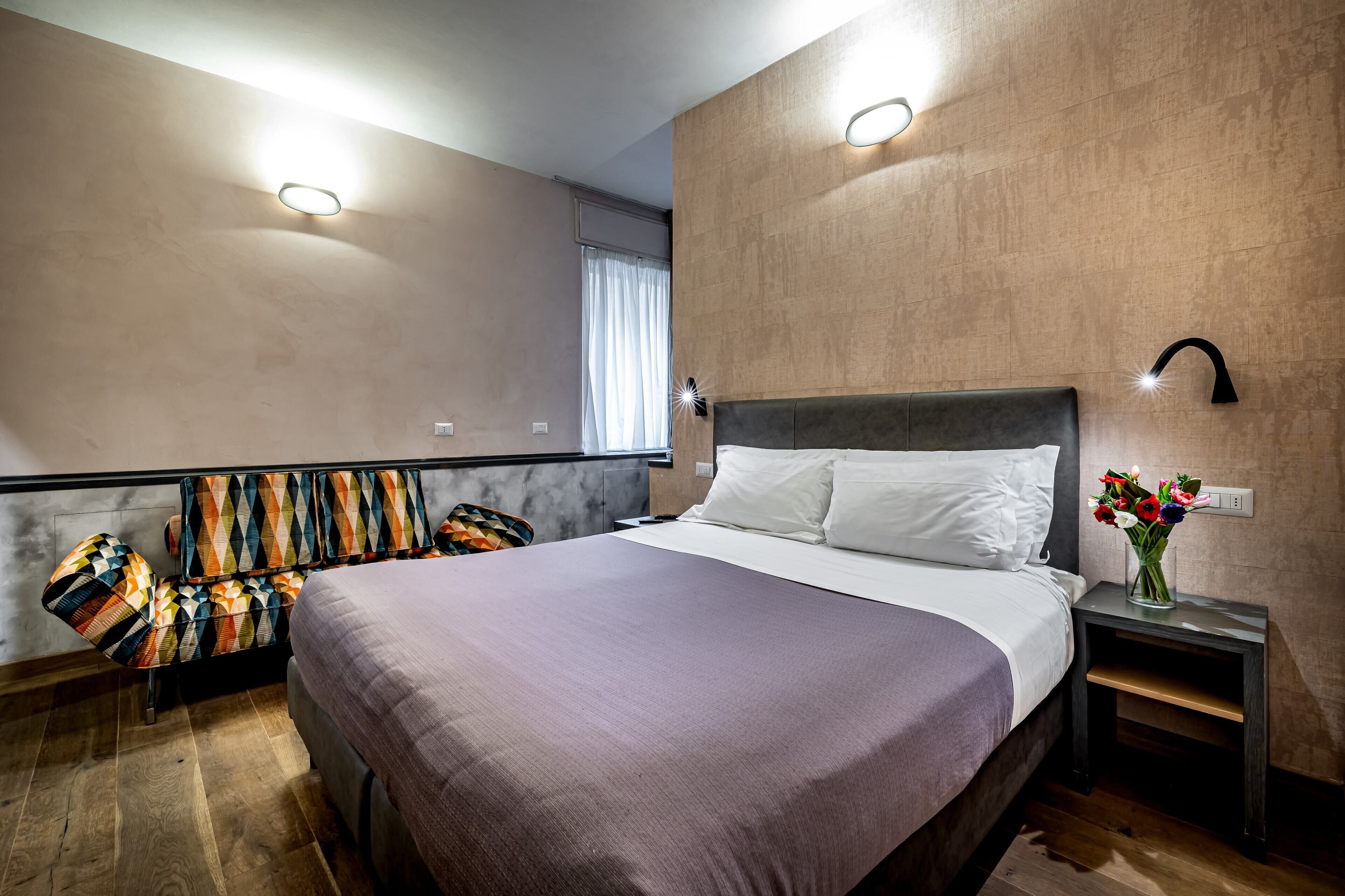 A modern bedroom with a large bed, a nightstand with a vase of flowers, and a unique patterned chair.
