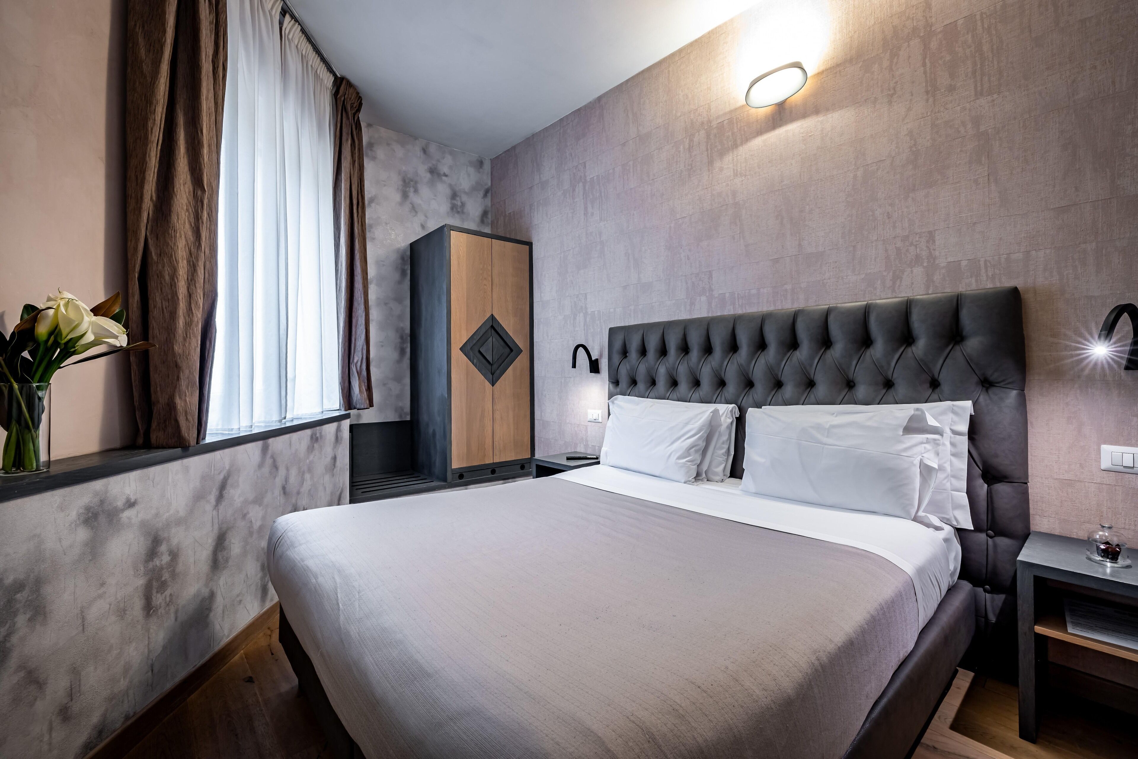 Une chambre d’hôtel moderne avec un grand lit, une armoire, une table de chevet et une petite table de nuit.