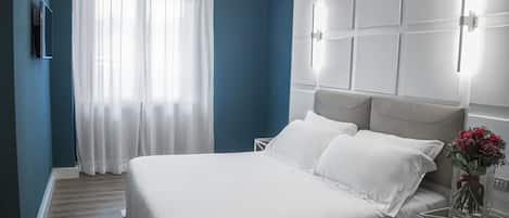 A modern bedroom with a large bed, a bedside table with a vase of flowers, and a wall-mounted light fixture.