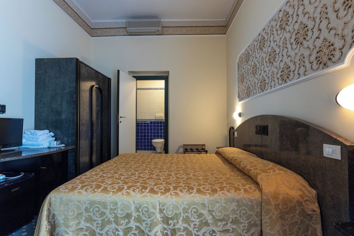 A hotel room with a bed, a desk with a television, a wardrobe, and a bathroom with a blue-tiled wall.