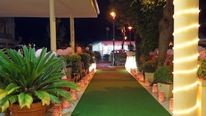 A pathway lined with potted plants and illuminated by string lights, leading to a building with a sign that reads "BARBERRY CHAMPIONS." - Hotel River (Rimini)