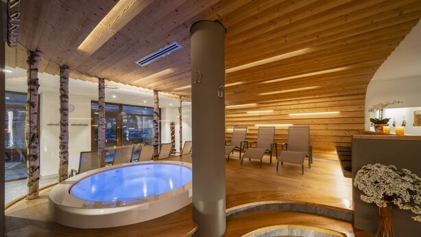 Un área de spa con jacuzzi, piso de madera y un espacio de descanso con sillas y una mesa.
